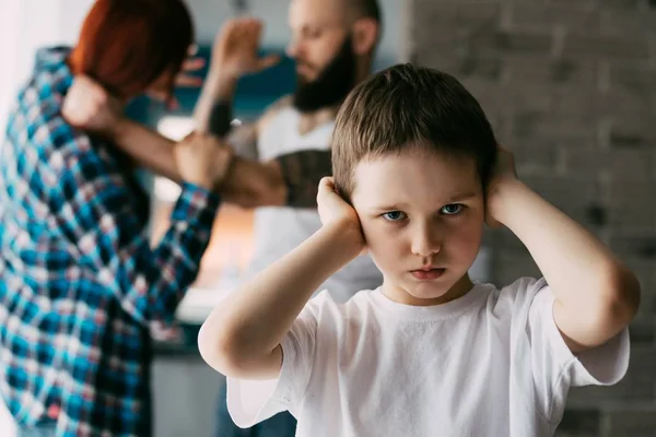 Verdrietig kind die betrekking hebben op zijn oren met handen tijdens ouders ruzie. — Stockfoto