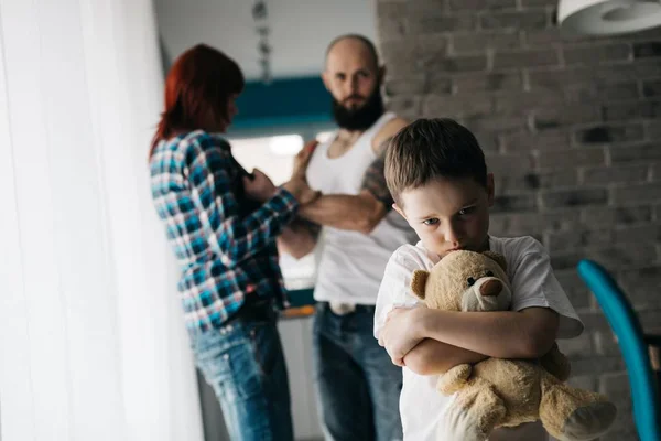 Triste criança abraçando seu ursinho durante a briga dos pais . — Fotografia de Stock