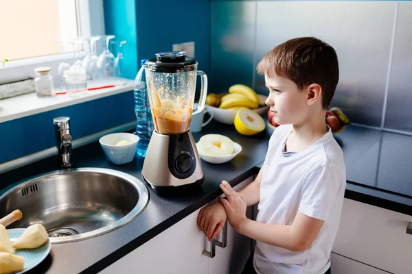 Счастливый ребенок готовит фруктовый коктейль на кухне — стоковое фото