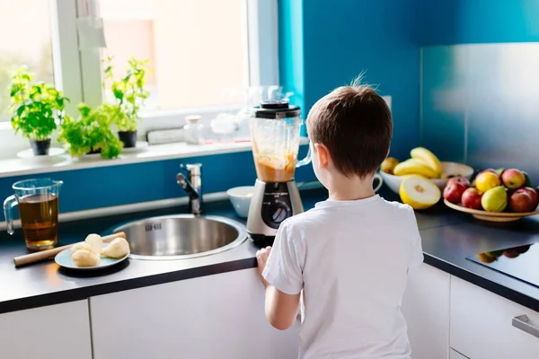 Счастливый ребенок готовит фруктовый коктейль на кухне — стоковое фото