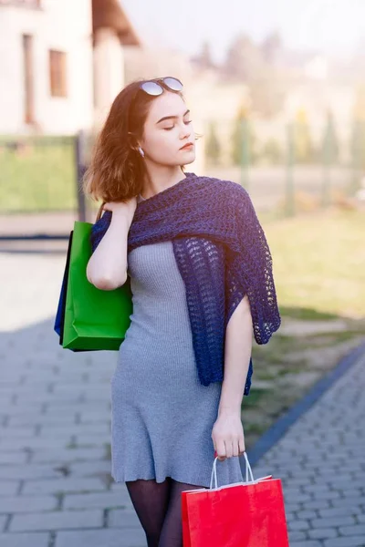 Girl in blue woolen shawl holding paper shopping bags.