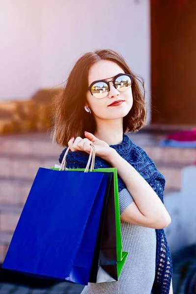 Girl in blue woolen shawl holding paper shopping bags.