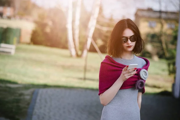 Fashion girl in pink woolen shawl using her smartphone — Stock Photo, Image