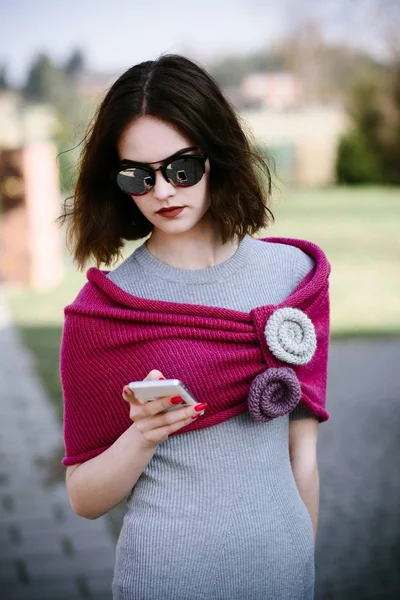 Fashion girl in pink woolen shawl using her smartphone — Stock Photo, Image