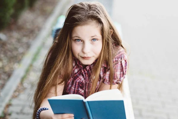 Дівчина читає книгу, лежачи на лавці в парку — стокове фото