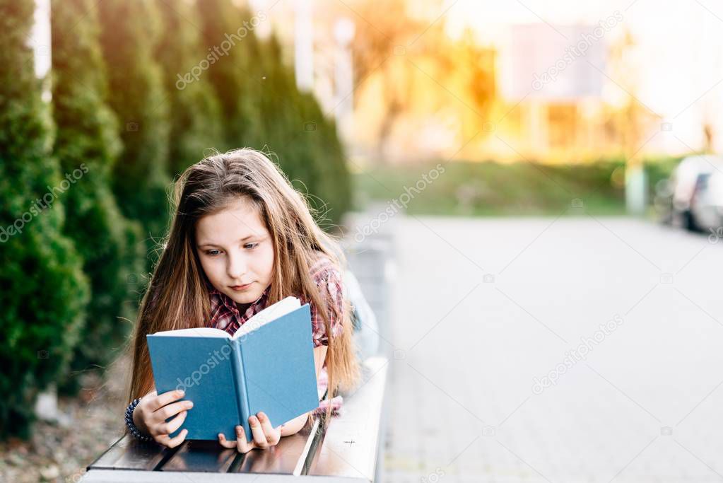 Girl reading a book while lying on the bench in the park
