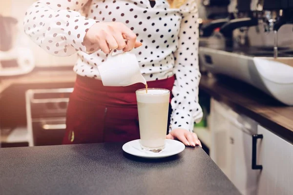 Woman barista pouring coffee to foamed milk.