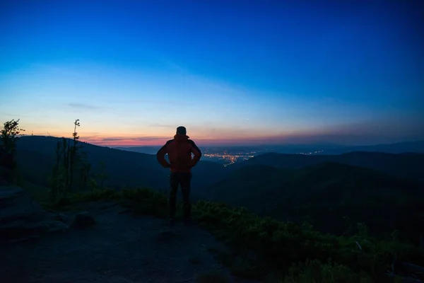 Homem turista de pé no topo da montanha observando luzes da cidade . — Fotografia de Stock