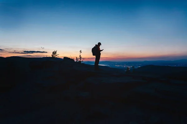 Homem turista de pé no topo da colina e usando seu smartphone . — Fotografia de Stock