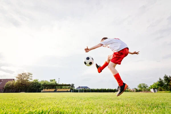 Восьмилетний мальчик пинает мяч на игровой площадке . — стоковое фото