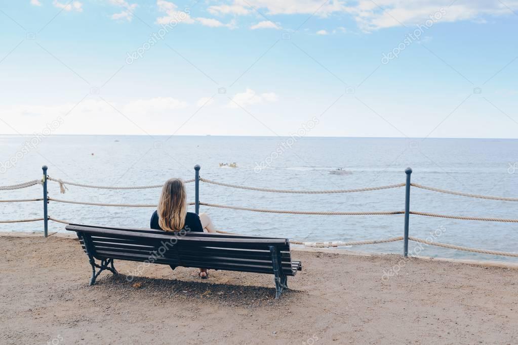 Woman sitting alone on the wooden bench in front of the ocean