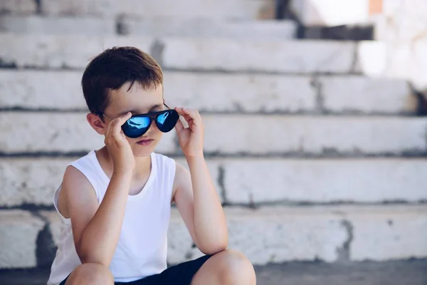 Lilla barn pojke bär solglasögon och sitter på gamla trappor — Stockfoto