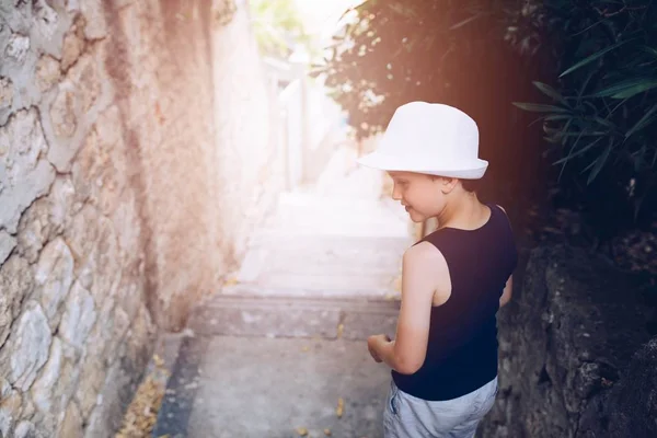 Kind in witte hoed lopen op smalle straat van de oude stad — Stockfoto