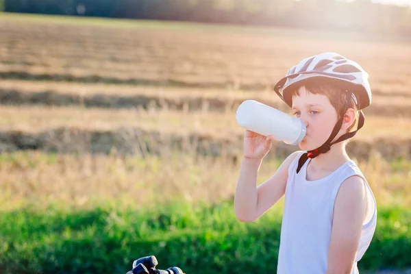 Chłopiec w kask rowerowy pije wodę mineralną — Zdjęcie stockowe