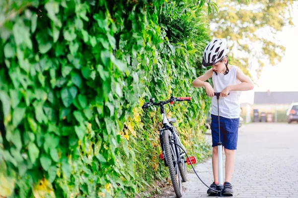 Щасливий хлопчик у велосипедному шоломі накачує колесо на своєму велосипеді — стокове фото