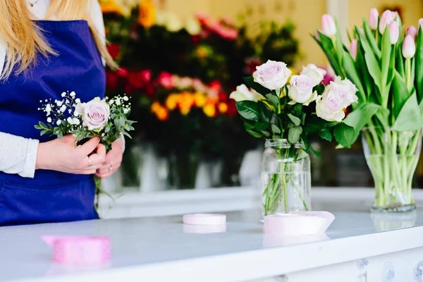 Woman owner of florist shop preparing bouquet of pink roses