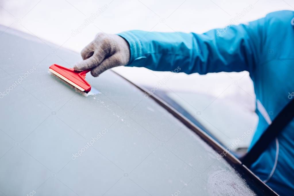 Woman scraping frozen front car windshield