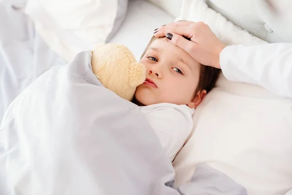 Arzt untersucht Kinderfieber mit der Hand auf der Stirn. — Stockfoto