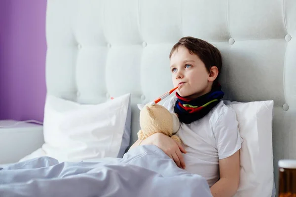 Больной восьмилетний мальчик в постели с термометром — стоковое фото