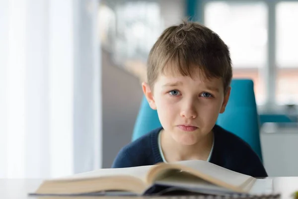 Trött 8 år gammal pojke gör sina läxor vid bordet — Stockfoto