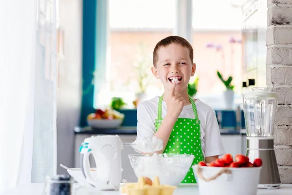 Glücklicher Junge probiert süßen Teig aus und bereitet einen Kuchen zu. — Stockfoto