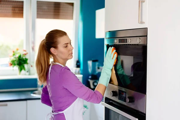橡胶手套清洁烤箱的年轻妇女 — 图库照片