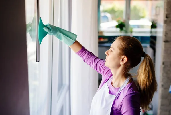 Ung kvinna i vitt förkläde rengöring windows. — Stockfoto