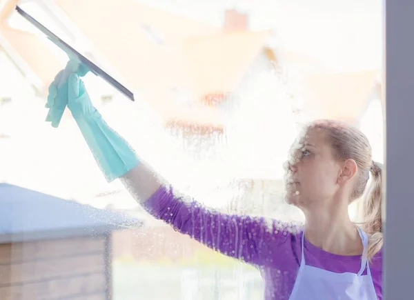 Mladá žena v bílé zástěře, mytí oken. — Stock fotografie