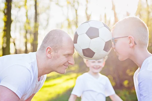 Молодой отец и сын играют с мячом на зеленой траве в парке . — стоковое фото