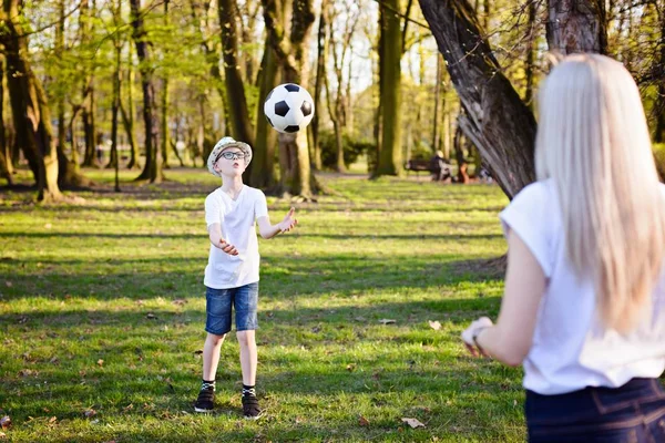 Mamma leker med boll med sina söner på grönt gräs i parken. — Stockfoto