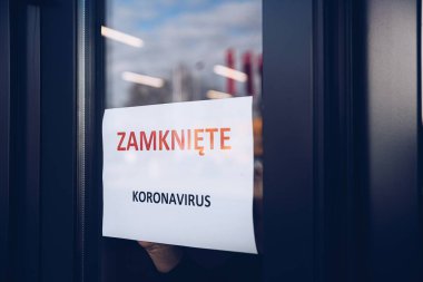 Kadın, Polonya dilinde koronavirüs nedeniyle mağazanın kapanışı hakkında bilgi içeren bir kart asıyor.
