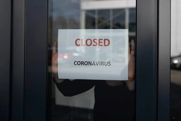 한 여성 이 코로나 바이러스때문에 가게 창문을 닫는다는 정보가 담긴 카드를 걸고 있습니다 — 스톡 사진