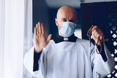 Tıbbi maskeli adam haç ve tespihle dua ediyor..