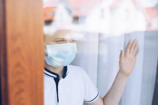 Ένα θλιμμένο παιδί με ιατρική μάσκα κοιτάζει από το παράθυρο. Καραντίνα — Φωτογραφία Αρχείου