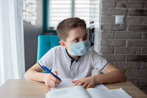 Criança com máscara médica protectora a fazer os trabalhos de casa. Escola fechada durante coronavírus — Fotografia de Stock