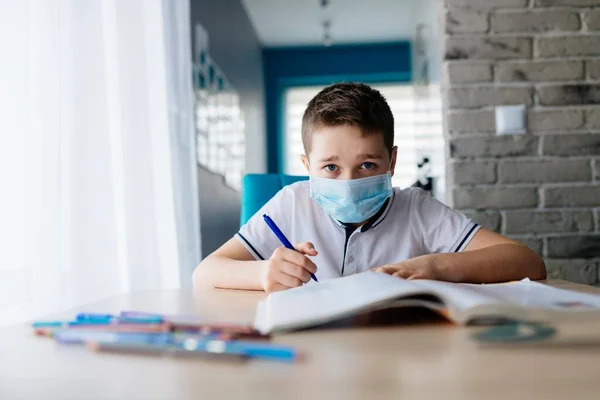 Criança com máscara médica protectora a fazer os trabalhos de casa. Escola fechada durante coronavírus — Fotografia de Stock