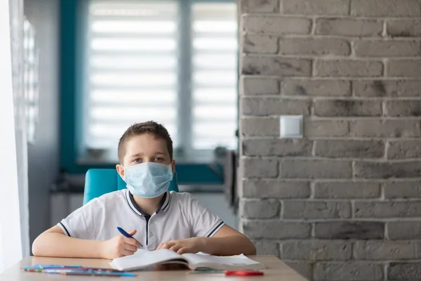 Criança com máscara médica protectora a fazer os trabalhos de casa. Escola fechada durante coronavírus — Fotografia de Stock