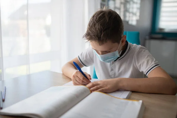 Дитина в захисній медичній масці робить домашнє завдання. Школа закрита під час коронавірусу — стокове фото