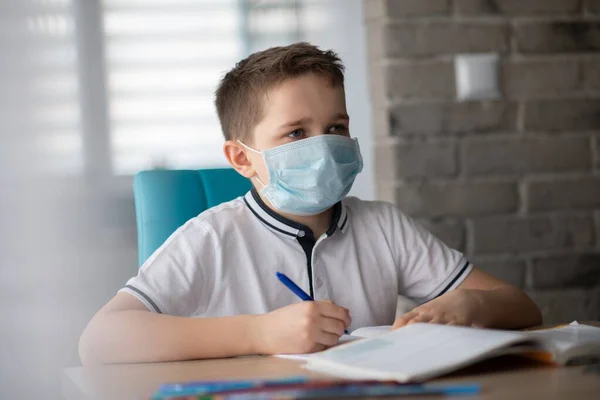 Anak bertopeng medis protektif melakukan pekerjaan rumahnya. Sekolah ditutup selama coronavirus — Stok Foto