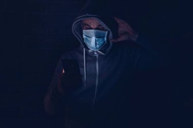 Korkmuş bir adam akıllı telefondan covid-19 koronavirüs hakkında bilgi okuyor. Coronavirus covid-19 salgını sırasında maskeli bir adam..