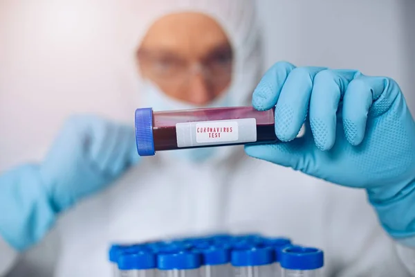 Científico en traje protector sosteniendo tubo de ensayo con sangre — Foto de Stock