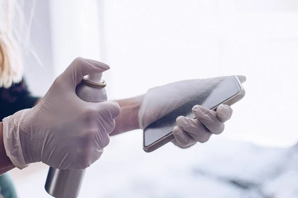 Femme désinfecte le téléphone avec un liquide désinfectant pulvérisé . — Photo