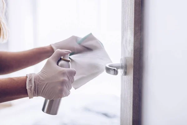 La mujer desinfecta la manija de la puerta con un líquido desinfectante . — Foto de Stock