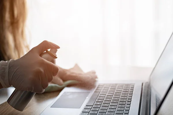 Woman disinfects the laptop keyboard with spray disinfectant liquid