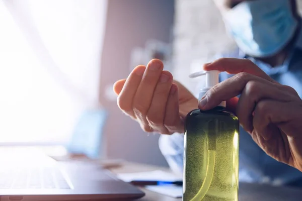Hombre en una oficina usando un ordenador y desinfecta sus manos con gel actibacterial — Foto de Stock