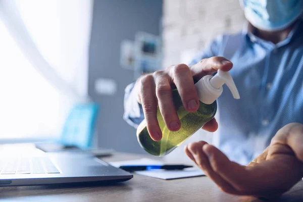 Чоловік в офісі за допомогою комп'ютера і дезінфікує руки антибактеріальним гелем — стокове фото