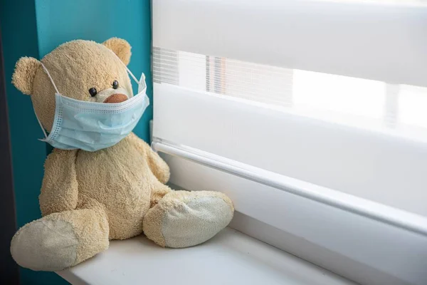 Oso mascota en el alféizar de la ventana de un hospital en una máscara médica . — Foto de Stock