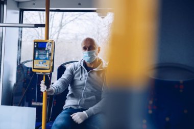Coronovirus covid-19 sırasında şehir otobüsüyle seyahat eden maskeli ve koruyucu eldivenli bir adam.