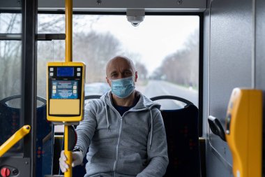 Coronovirus covid-19 sırasında şehir otobüsüyle seyahat eden maskeli ve koruyucu eldivenli bir adam.