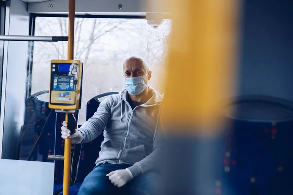 Mann mit Maske und Schutzhandschuhen unterwegs im Stadtbus während Coronovirus covid-19 — Stockfoto